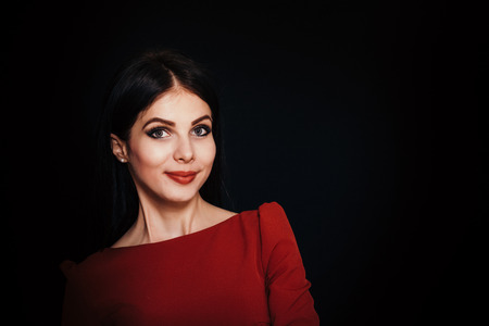 A beautiful woman with black straight hair and blue eyes in a burgundy dress on a dark background. Close-up. Space for textの写真素材