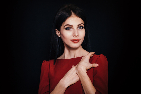 A beautiful woman with black straight hair and blue eyes in a burgundy dress on a dark background. Close-up. Space for textの写真素材