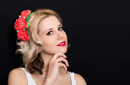 Woman with blonde laying and rimmed with red flowers on a dark background. Close-up. Space for textの写真素材