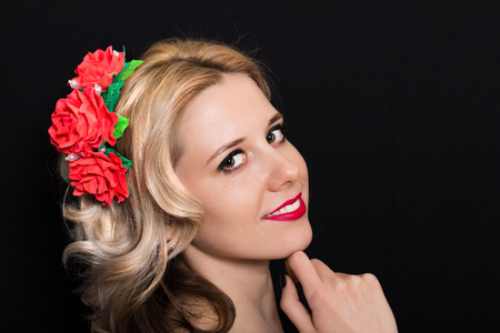Woman with blonde laying and rimmed with red flowers on a dark background. Close-up. Space for textの写真素材