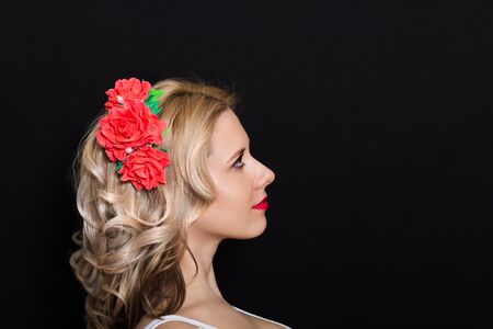 Woman with blonde laying and rimmed with red flowers on a dark background. Close-up. Space for textの写真素材