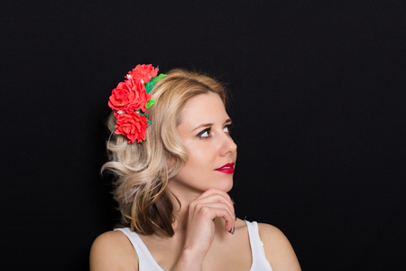 Woman with blonde laying and rimmed with red flowers on a dark background. Close-up. Space for textの写真素材