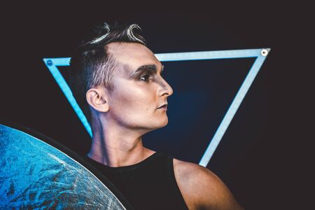 Portrait of beautiful young man with modern hairstyle, artistic multicolor makeup. Studio shot. Black backgroundの写真素材