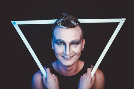 Portrait of beautiful young man with modern hairstyle, artistic multicolor makeup. Studio shot....