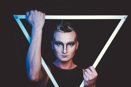 Portrait of beautiful young man with modern hairstyle, artistic multicolor makeup. Studio shot. Black backgroundの写真素材