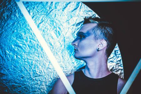 Portrait of beautiful young man with modern hairstyle, artistic multicolor makeup. Studio shot. Black backgroundの写真素材