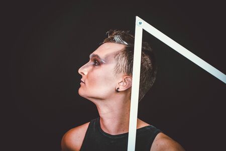 Portrait of beautiful young man with modern hairstyle, artistic multicolor makeup. Studio shot. Black backgroundの写真素材