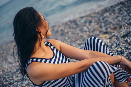 A woman sits on the sand and looks at the sea close upの写真素材