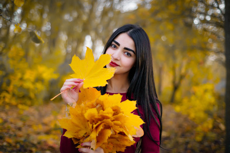 Beautiful brunette woman in autumn foliage smiling.の写真素材
