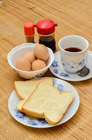 Breakfast with coffee, 2 slices of bread, half-boiled eggs, soy sauce and white pepperの写真素材