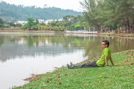 A young man sitting alone near the water