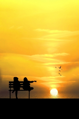 Silhouette of two friends sitting on wood bench near beach staring at flying birdの写真素材