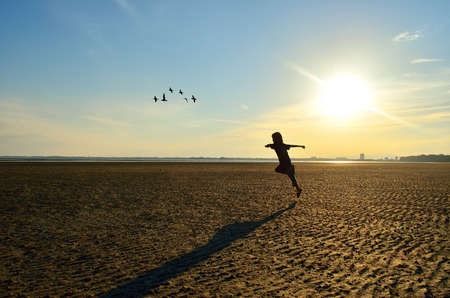 Silhouette of kid running on beach at sunsetの写真素材