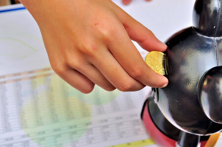 saving money, female hand is putting coin into coins toy bankの写真素材