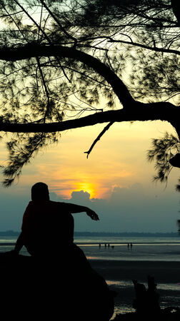 Silhouette of man sitting on the rock looking for the sun goes downの写真素材