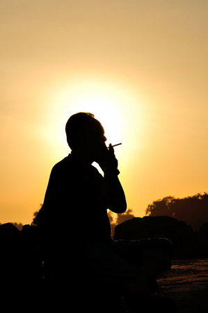 A man smoking cigarette over golden sunsetの写真素材