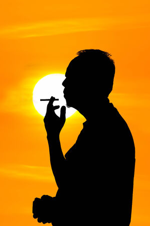 A man smoking cigarette over golden sunsetの写真素材