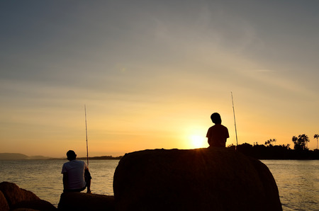 Silhouette of Father and son fishing in ocean surf at sunset.の写真素材