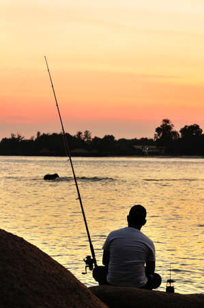Fisherman silhouette on the beach at colorful sunsetの写真素材