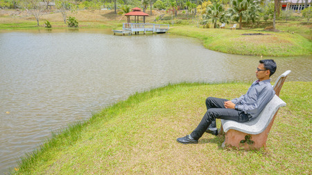 A young man sitting on the chair near the lake seeking for the peaceの写真素材