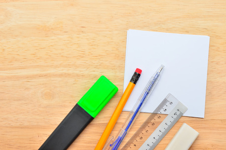 Blank sticky note with pen, pencil, ruler, highlight market and eraser on office wooden table. Above...