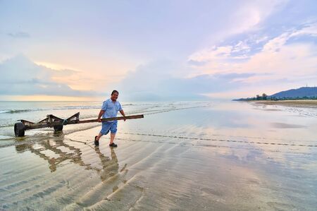 KUANTAN, MALAYSIA - 9 NOV 2013 - A man pull the boat puller from the sea at Beserah beach, Kuantan, Malaysia at 9 November 2013. Fishermen are the main jobs for villagers at Kuantan, Pahang, Malaysia.のeditorial素材