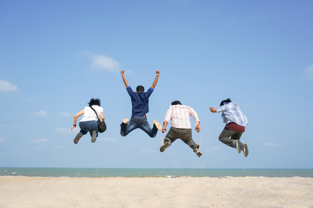 Young friends having fun on the beach and jumping against a backdrop of a blue skies. Seen in the picture, motion blur on the feet because of acrobatic movementsの写真素材