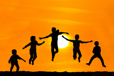 Silhouette of boy and girl jumping over sunsetの写真素材