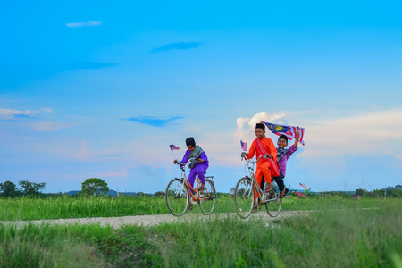 independence Day concept - Two happy young local boy riding old bicycle at paddy field holding a Malaysian flagの写真素材