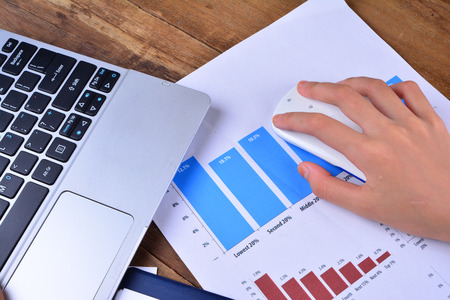 Hand on keyboard and mouse with graph, chart on wooden table