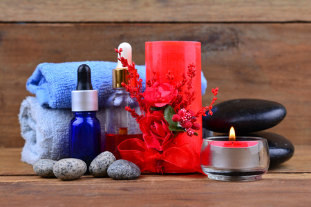 Red romantic candle and spa oil with towel and zen stone on wooden tableの写真素材