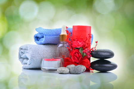 Red romantic candle and spa oil with towel and zen stone over green blur bokeh backgroundの写真素材