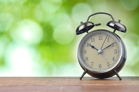 larm clock on wood with blurry green bokeh in background. Concept of time