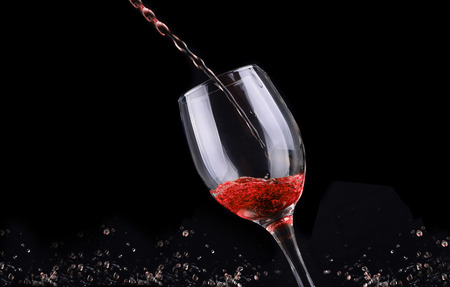 Red wine pouring into a wine glass. Isolated on black backgroundの写真素材