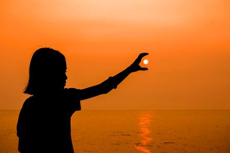 Portrait of young woman as silhouette and hand holding the sunの写真素材
