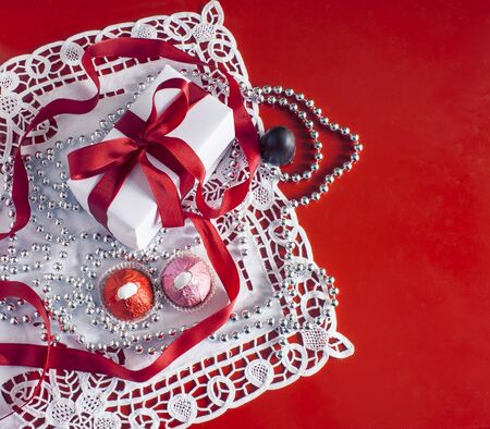 Valentine's Day, gift box with a red ribbon, bead, candies and white vintage lace in red background.の写真素材
