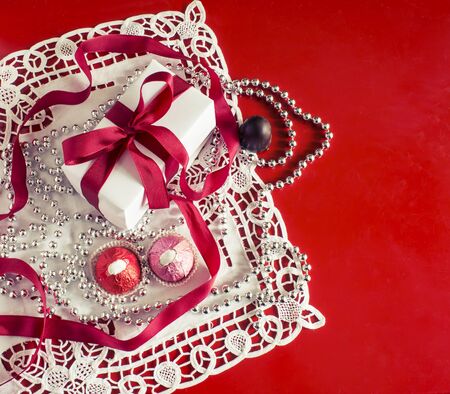Valentine's Day, gift box with a red ribbon, bead, candies and white vintage lace in red background.の写真素材