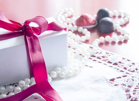 Valentine's Day, gift box with a red ribbon, pearl bead, candies and white vintage lace in red background.の写真素材