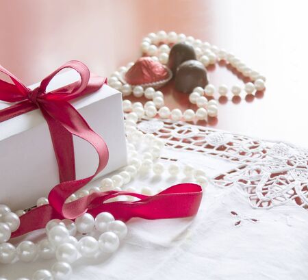Valentine's Day, gift box with a red ribbon, pearl bead, candies and white vintage lace in red background.の写真素材