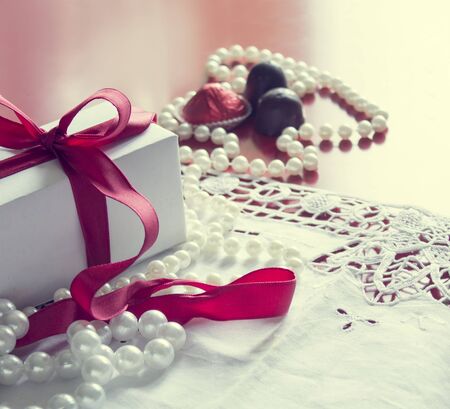 Valentine's Day, gift box with a red ribbon, pearl bead, candies and white vintage lace in red background.の写真素材