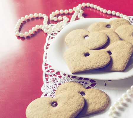 Hearts cookies on white dish with lace and pearl on red background, romantic love backdrop for Valentine's day.の写真素材