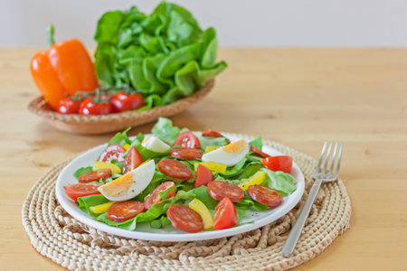 Fresh spicy Spanish chorizo and egg salad in white plate with a basket of vegetables and wooden table backgroundの写真素材