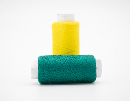 Sewing thread and bobbin in Dark Cyan and yellow on isolated white backgroundの写真素材