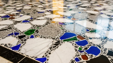 A close-up view of a mosaic floor featuring a mix of white, blue, green, black, and brown tiles arranged in a random pattern, with a reflective surface that adds depth and visual interest to the compoの写真素材