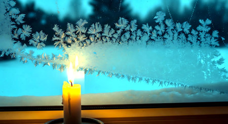 Burning candle on the background of the window with snow and frostの素材