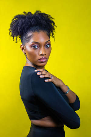 Young black woman poses in front of a yellow backdrop, Black woman loving herself, Black woman wearing all blackの写真素材