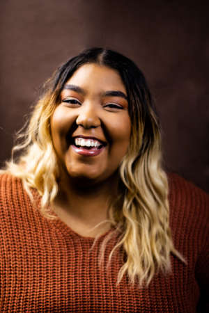 Black girl wearing burnt orange sweater with brown backdrop, Black girl wearing a sweater, Mixed girl wearing burnt orange sweater with brown backdrop, Mixed girl wearing a sweaterの写真素材