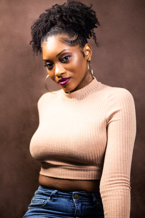 Black woman wearing brown sweater sitting down posing sideways with hopped earrings, Black woman with natural hairの写真素材