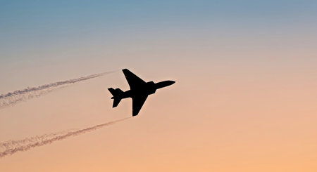 Silhouette of a military airplane flying in the sky at sunsetの写真素材