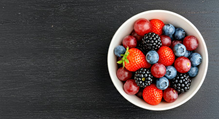 Mix of fresh berries in bowl on black wooden background, top viewの写真素材